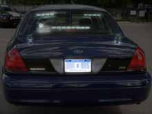 Short police radio antenna on trunk - Rear-facing radar - Light flashers in rear window - Government license plate - Police Interceptor badge 